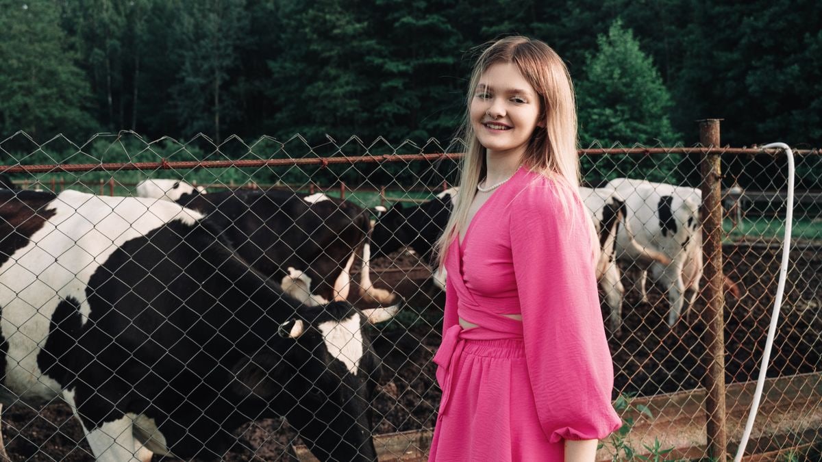 Teen girl in a pink dress smiles next to cows at a rural farm.